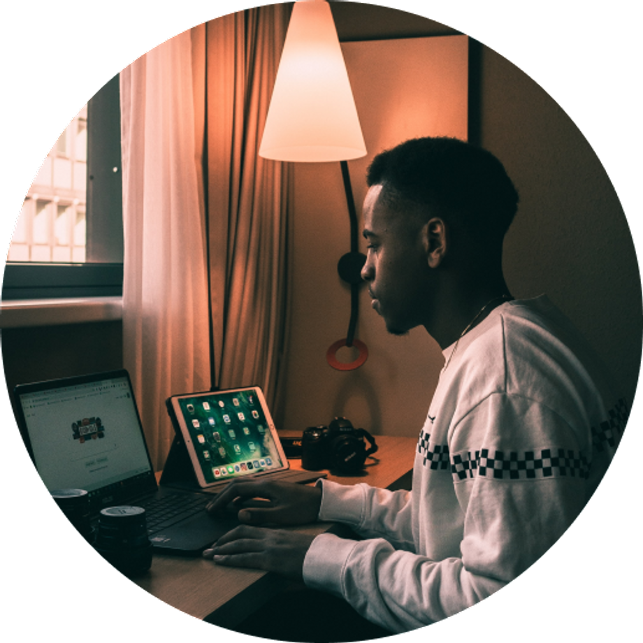 Black man using his laptop and tablet with a low-lit lamp